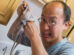 A man with glasses looks surprised and makes a humorous expression while holding a raw octopus in the kitchen. The octopus appears to be squirming in his hand