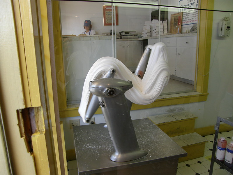 A machine pulling and stretching saltwater taffy in a candy shop with a worker visible in the background.