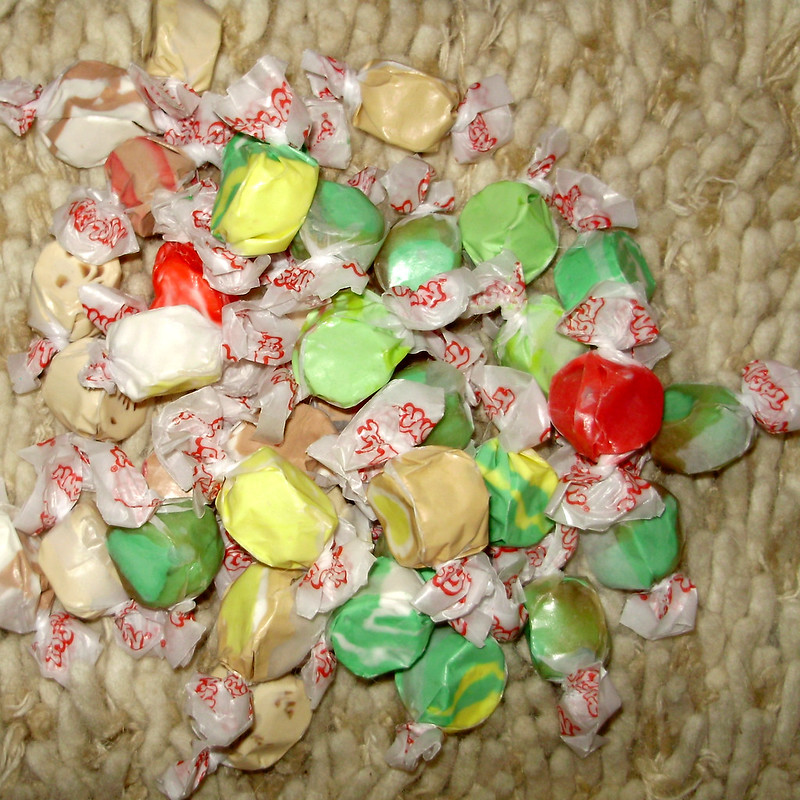 A pile of saltwater taffy candies in beige, green, red, and yellow, individually wrapped.