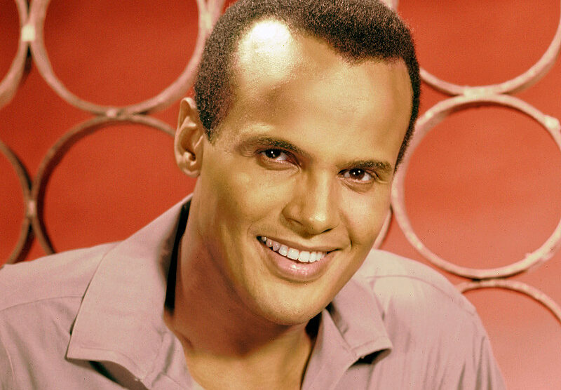 A close-up portrait of a smiling man with short hair, wearing a light-colored shirt. The background features circular patterns in a warm hue.
