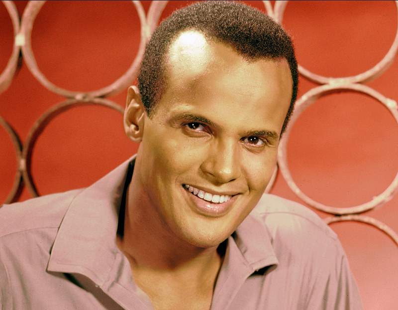 A close-up portrait of a smiling man with short hair, wearing a light-colored shirt. The background features circular patterns in a warm hue.