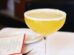 A classic Margarita cocktail served in a coupe glass with a salted rim, resting on a white tablecloth next to a menu and a plate.