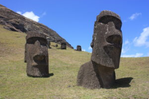 Close-up of two Moai statues on a grassy slope under a blue sky, partially buried in the ground at Rano Raraku quarry on Easter Island.