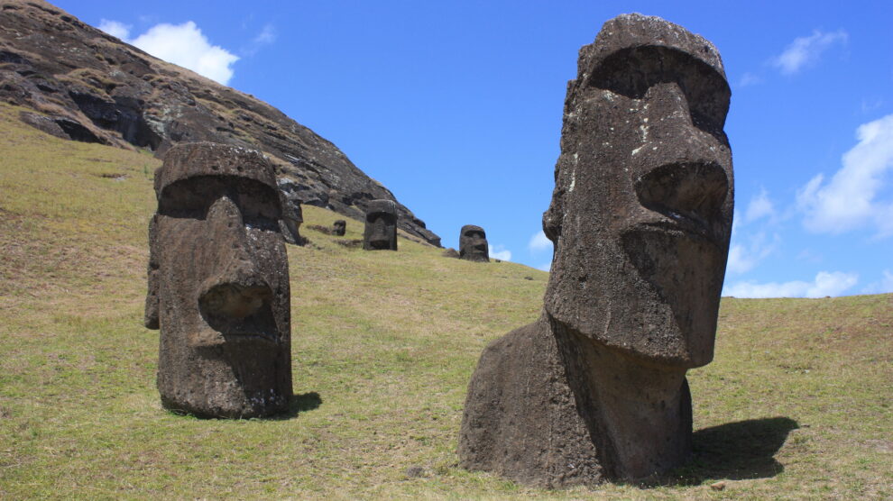 Close-up of two Moai statues on a grassy slope under a blue sky, partially buried in the ground at Rano Raraku quarry on Easter Island.