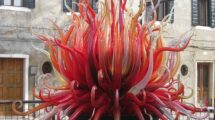 A vibrant glass sculpture in Murano, Italy, with red, orange, and yellow glass spikes resembling flames in front of a traditional Venetian building.