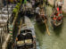 Gondolas on a narrow canal in Venice, with gondoliers navigating and tourists seated, surrounded by buildings and a small bridge.