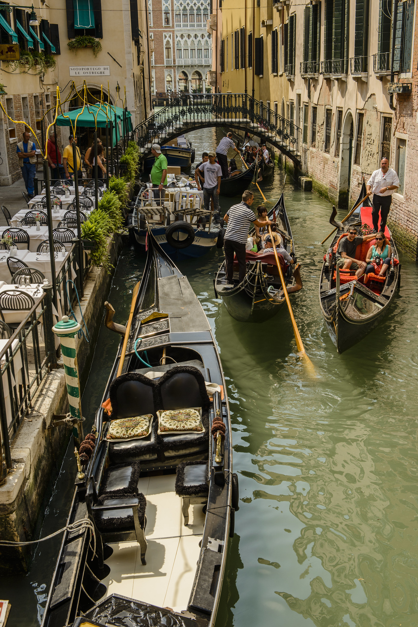Gondolas on a narrow canal in Venice, with gondoliers navigating and tourists seated, surrounded by buildings and a small bridge.