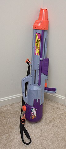 A large vintage Super Soaker CPS 2000 water gun with a purple and gray color scheme, leaning against a wall.