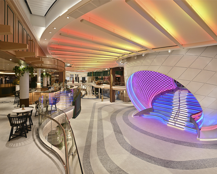 A modern cruise ship promenade on the Icon of the Seas, featuring brightly colored lighting, a sculptural centerpiece, and shops including a Starbucks, offering a sleek and futuristic environment for passengers.