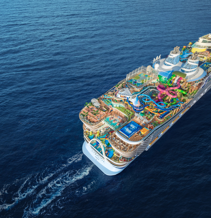  Aerial view of the Icon of the Seas, a large, modern cruise ship with multiple decks featuring pools, water slides, and entertainment areas, sailing in the ocean.