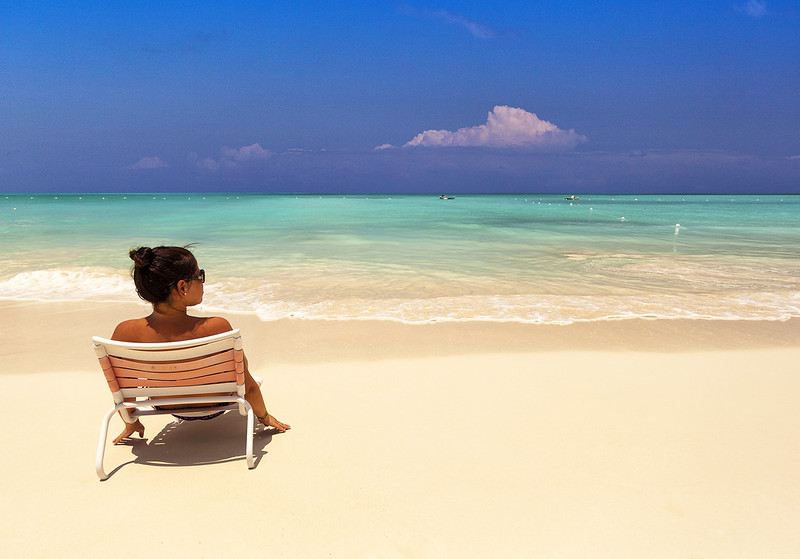 A person sitting in a lounge chair facing the clear turquoise waters of Grace Bay, Turks and Caicos, under a blue sky.