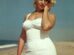 Marilyn Monroe on a beach in a white swimsuit, posing gracefully with her hand near her face, against an ocean backdrop