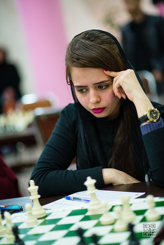 A woman wearing a black headscarf and sweater concentrates on a chess game, representing the importance of careful decision-making.