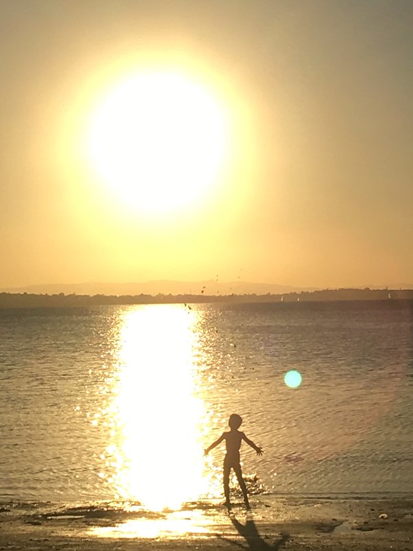A child silhouetted against a golden sunset plays at the water's edge, symbolizing the joy and freedom of paradise living.