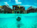 A person snorkeling underwater with overwater bungalows in the Maldives in the background.
