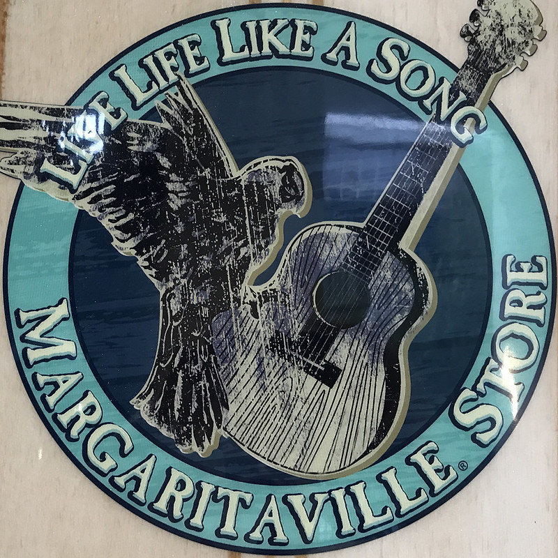 Margaritaville Store sign featuring a parrot flying across an acoustic guitar, with the phrase 'Live Life Like A Song.'