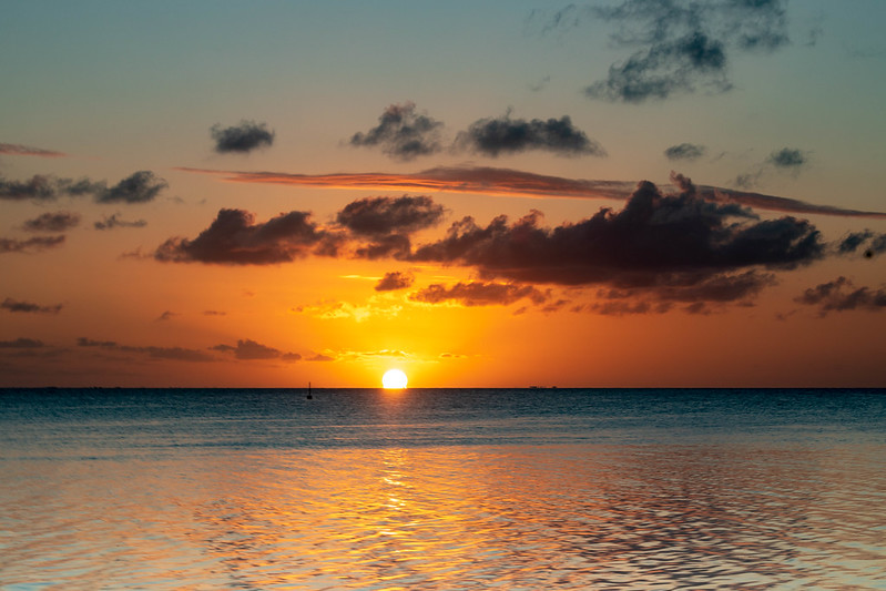Sunset at Matira Beach, Bora Bora, with the sun near the horizon, orange sky, and reflections on the tranquil water