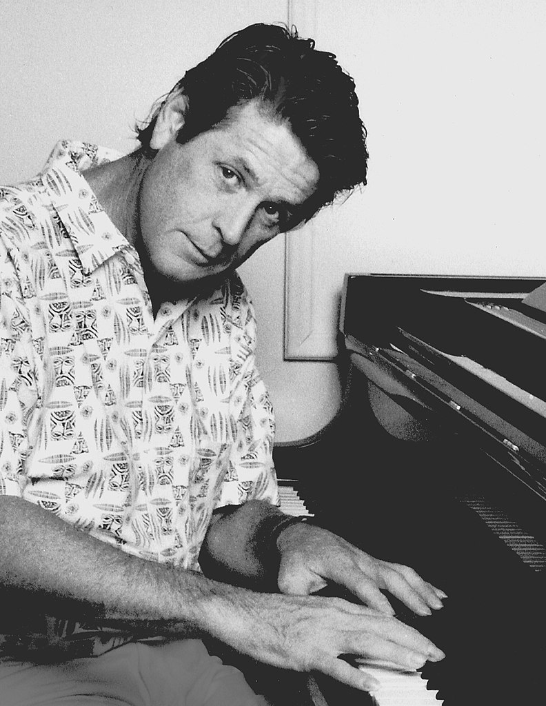 Brian Wilson of the Beach Boys, wearing a patterned shirt, playing the piano with an introspective expression.