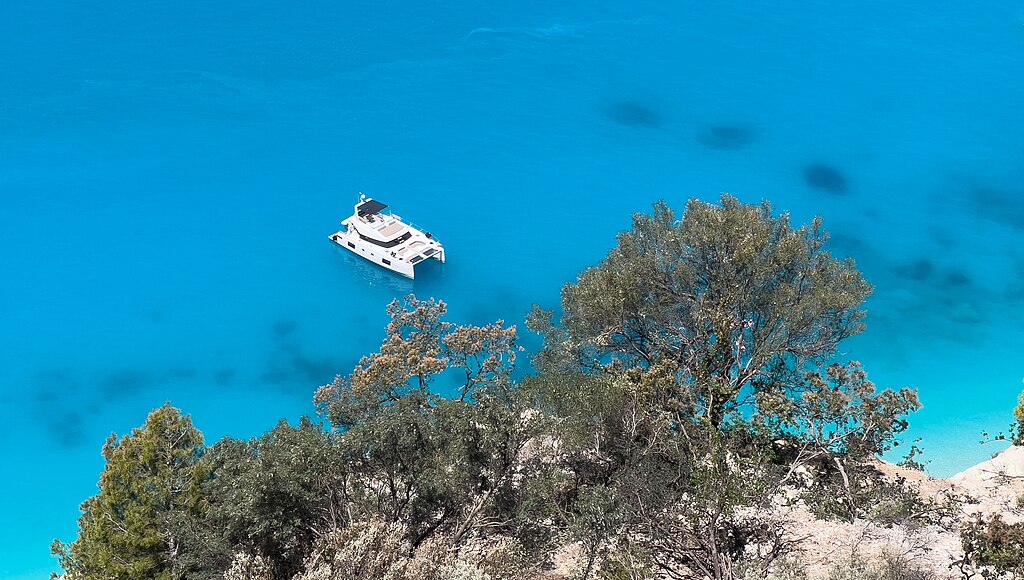 A boat floating in the clear turquoise waters of Egremni Beach, Greece, with greenery in the foreground.