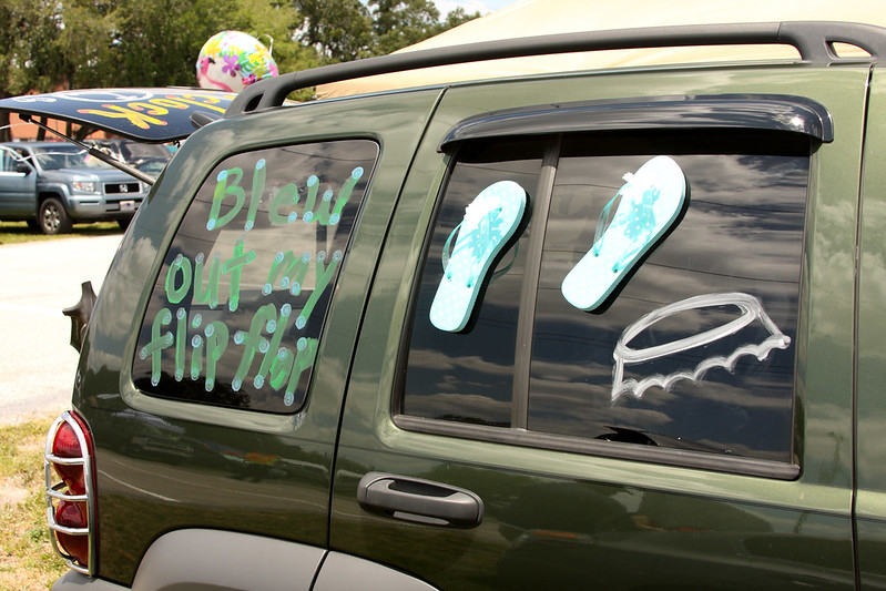 A green SUV with windows decorated in a Jimmy Buffett theme, featuring the phrase “Blew out my flip-flop” and drawings of flip-flops.