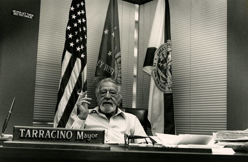 Black-and-white photo of Captain Tony Tarracino sitting at his desk as Mayor of Key West, holding a cigarette, embodying the charisma that inspired Jimmy Buffett’s song "Last Mango in Paris."