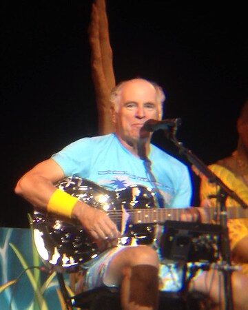 Jimmy Buffett performing on stage with a resonator guitar, showcasing his relaxed and heartfelt style inspired by his connection to Captain Tony Tarracino.