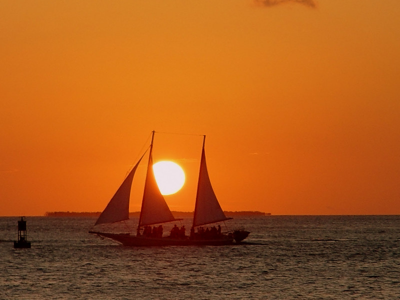 Silhouette of a sailboat with passengers against a vibrant orange sunset over the ocean in Key West, Florida.