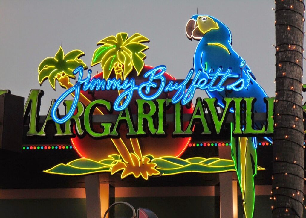 A brightly lit neon sign for Jimmy Buffett’s Margaritaville, featuring palm trees, a parrot, and tropical colors