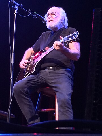 Robert Hunter seated and playing guitar on stage during a live performance at Town Hall in 2013.