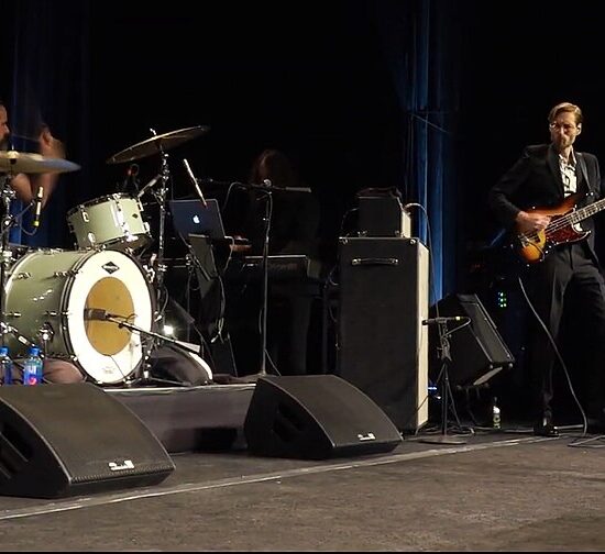 The Killers performing live in Las Vegas, featuring Brandon Flowers singing, Ronnie Vannucci Jr. on drums, and Mark Stoermer on bass.