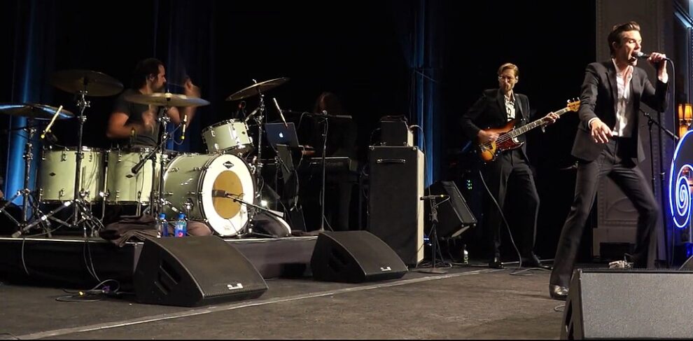 The Killers performing live in Las Vegas, featuring Brandon Flowers singing, Ronnie Vannucci Jr. on drums, and Mark Stoermer on bass.
