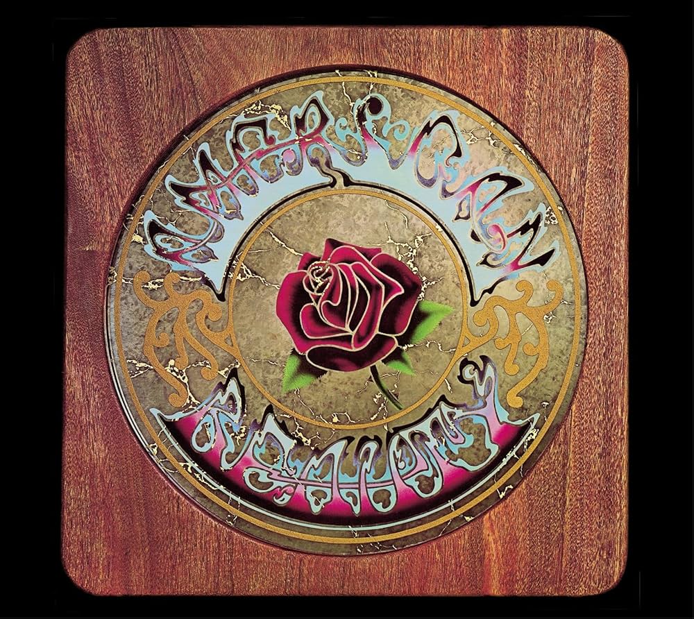 The album cover of American Beauty by the Grateful Dead, showcasing a detailed rose design surrounded by ornate patterns on a woodgrain background.