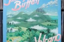 Jimmy Buffett's Volcano album cover featuring illustrated green mountains, a smoking volcano, tropical foliage, and a blue sky with scattered clouds. The album title "Volcano" is displayed in pink and white letters, with "Jimmy Buffett" prominently written at the top in a bold, stylized font. The vinyl cover is positioned in front of a shelf filled with records. Let me know if you’d like any modifications! 🎶🌋